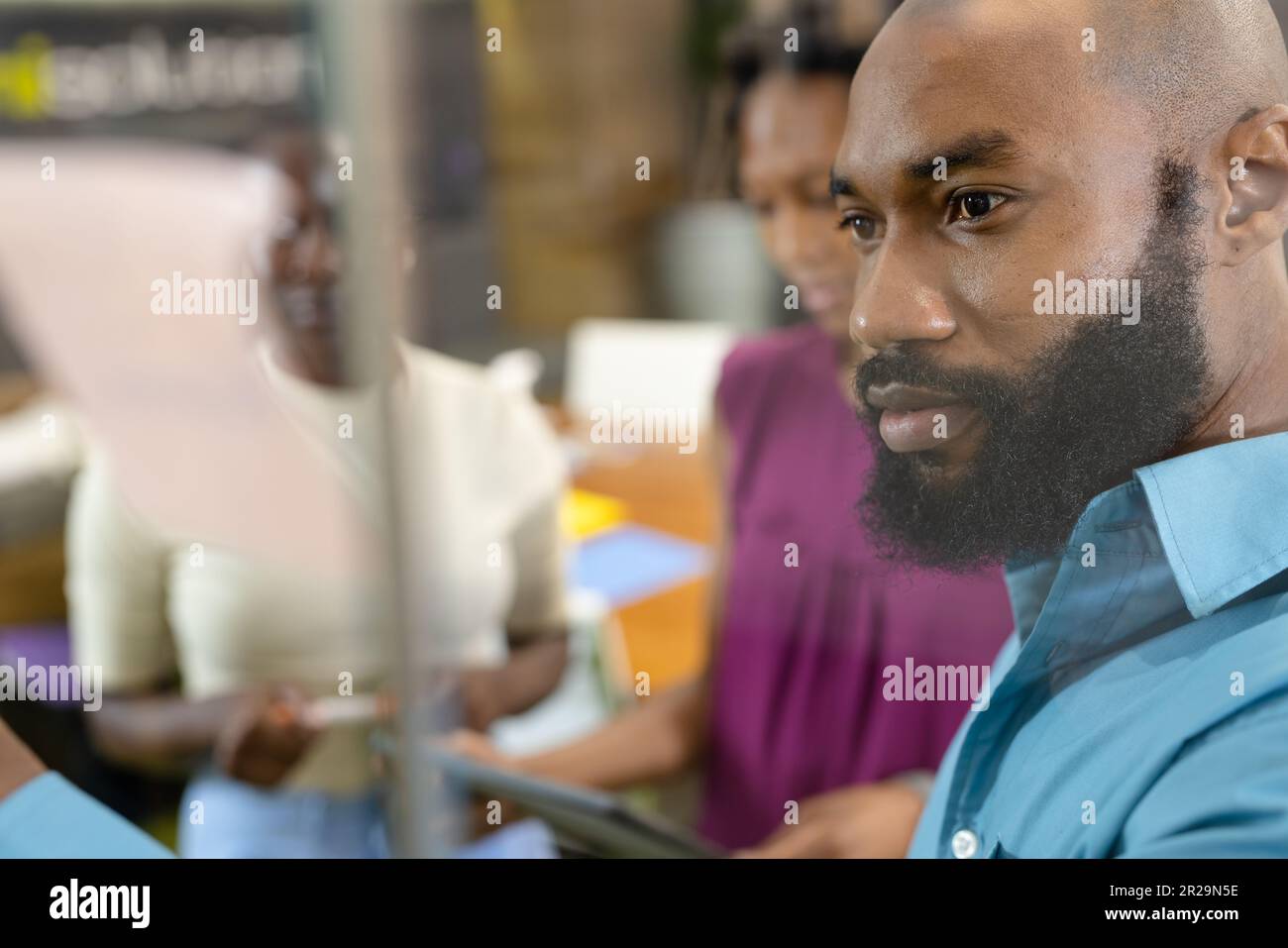 Primo piano di un uomo d'affari afro-americano che discute con colleghi donne visti attraverso una parete di vetro Foto Stock