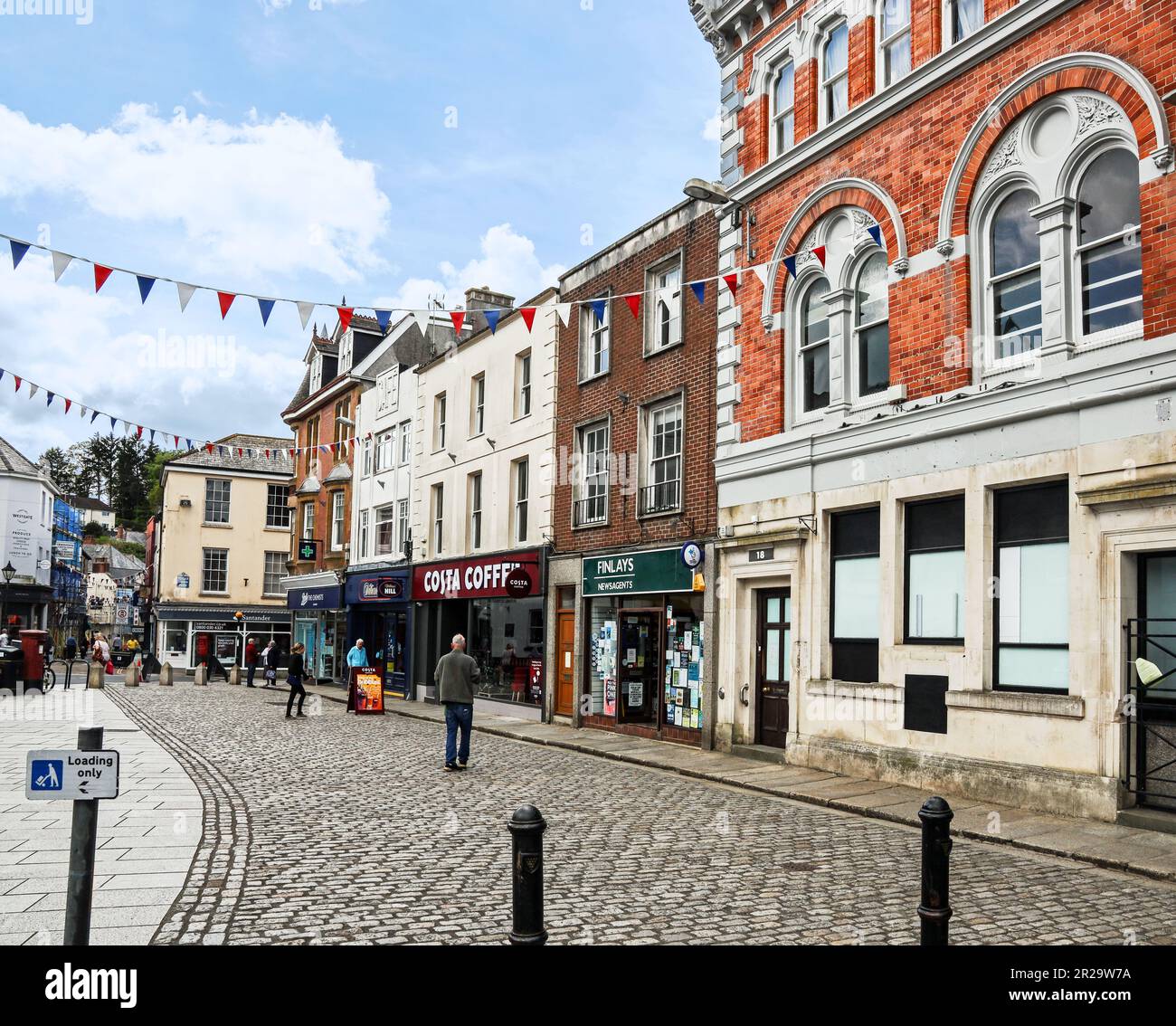 Negozi ai margini della Piazza della Città, nell'antica cittadina di Launceston, in Cornovaglia. Nomi ben noti sulla strada principale. Foto Stock