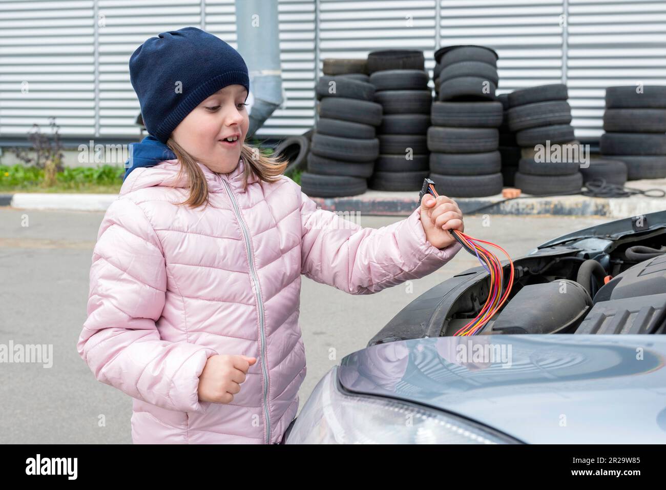 Un bambino felice sta levandosi in piedi vicino ad una macchina con un filo nelle sue mani. La bambina lavora in garage. Foto Stock