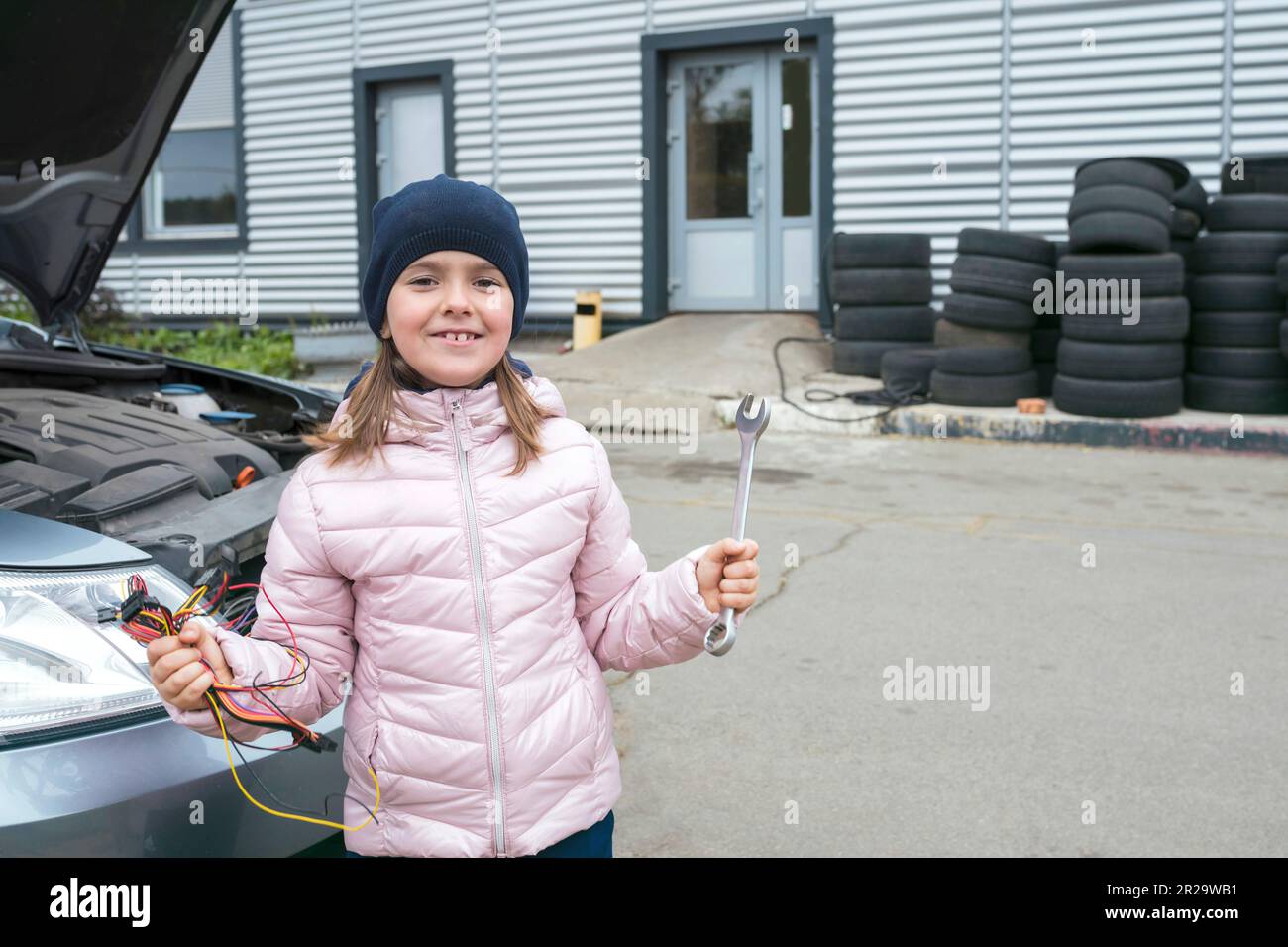 Una ragazza piccola felice con una chiave su una priorità bassa del servizio dell'automobile. Servizio di riparazione Foto Stock