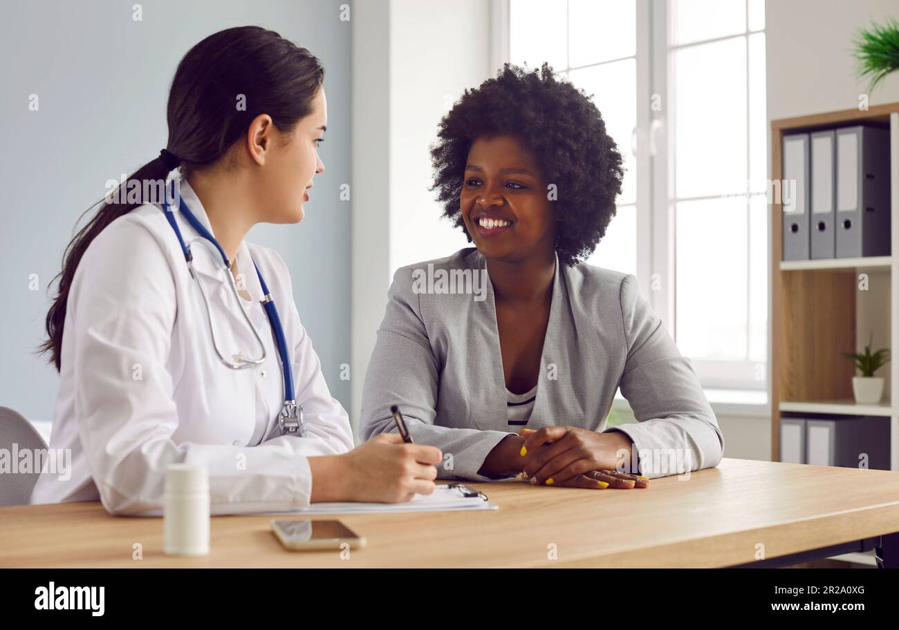 Medico che parla con una paziente donna e la scrittura delle sue lamentele in notebook. Foto Stock