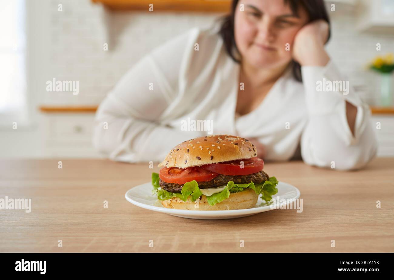 Donna sovrappeso che guarda l'hamburger che si trova davanti a lei Foto Stock