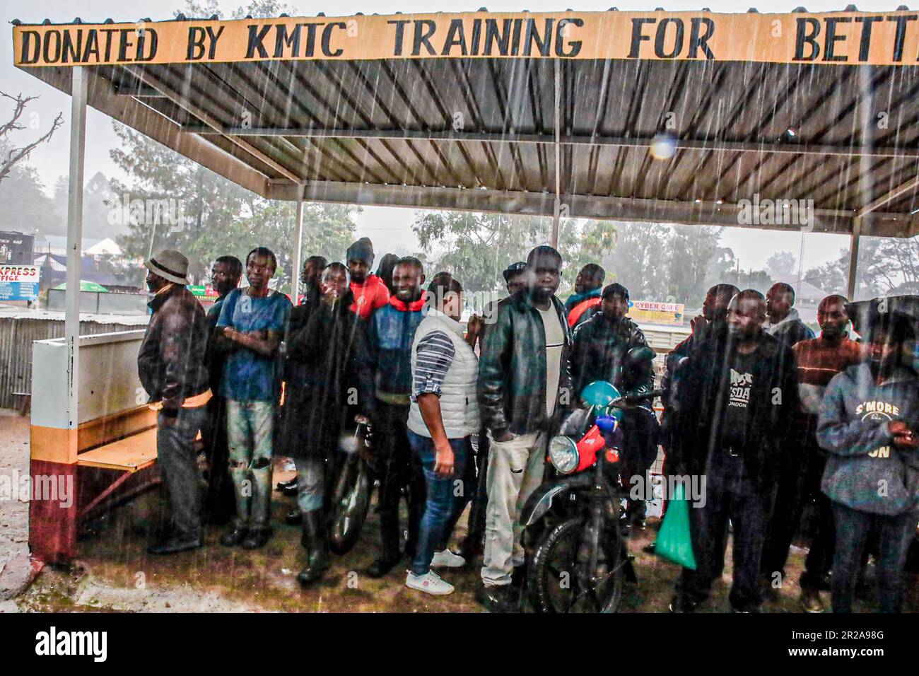 Gli abitanti del posto si rifugiano all'ombra durante le forti piogge a Kibera Slum. I residenti di Nairobi camminano per le strade alla ricerca di pascoli più verdi nel mezzo dell'alto costo della vita e delle turbolenze economiche. Foto Stock