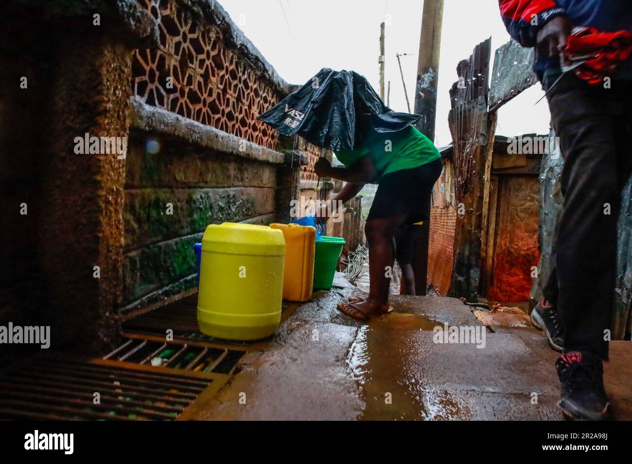 Una donna raccoglie l'acqua piovana durante le forti piogge di Kibera Slum. I residenti di Nairobi camminano per le strade alla ricerca di pascoli più verdi nel mezzo dell'alto costo della vita e delle turbolenze economiche. Foto Stock