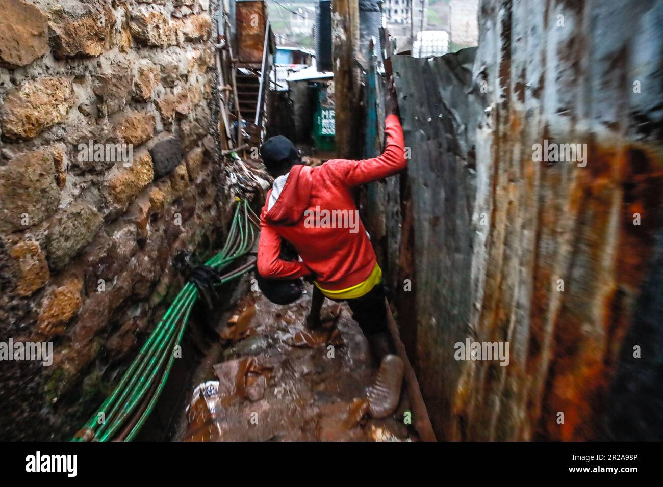 Un uomo scivola mentre si dirige a casa durante le forti piogge in Kibera Slum. I residenti di Nairobi camminano per le strade alla ricerca di pascoli più verdi nel mezzo dell'alto costo della vita e delle turbolenze economiche. Foto Stock