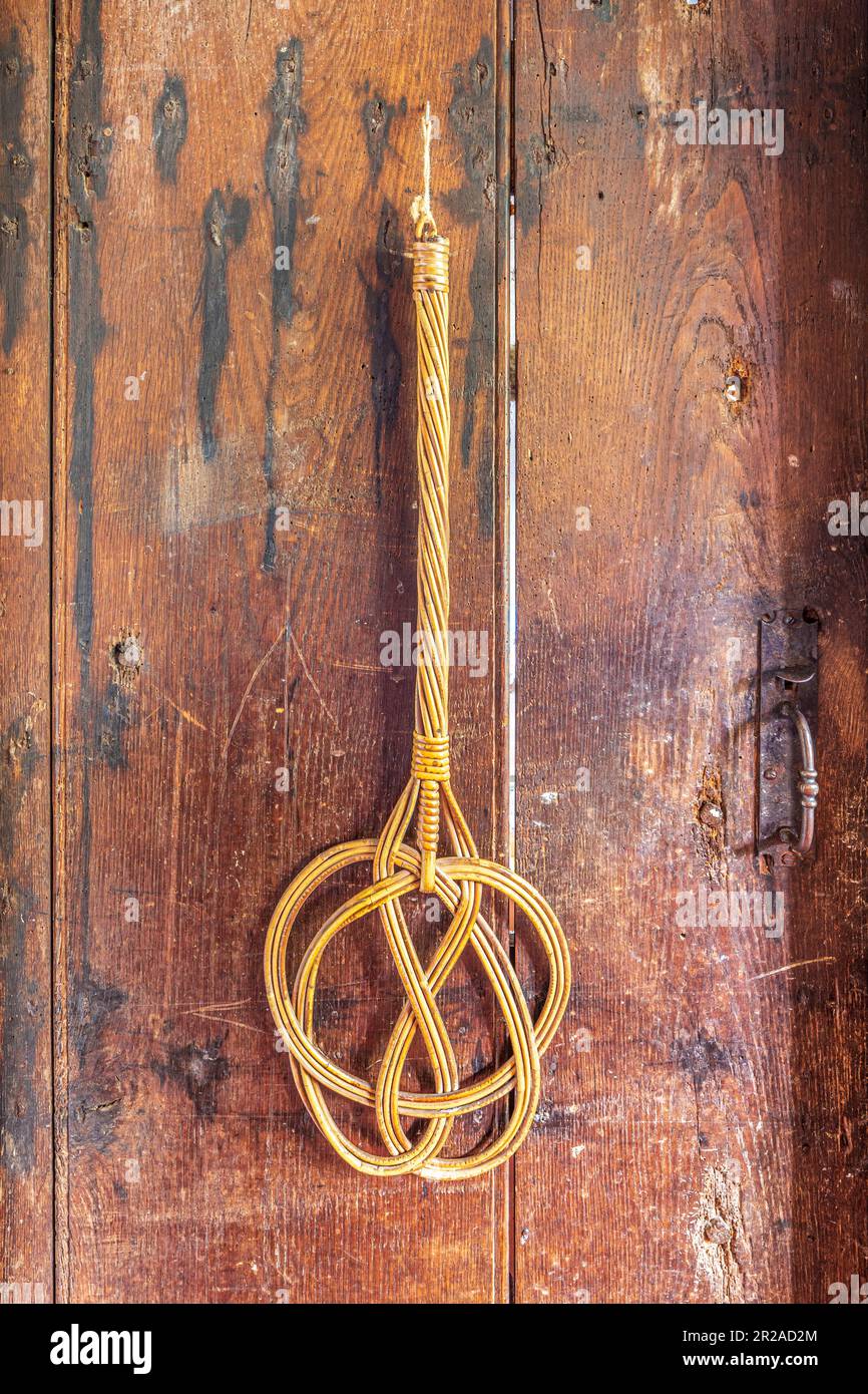 Una tradizionale frusta per tappeti in vecchio stile appesa ad una vecchia porta di legno. Foto Stock