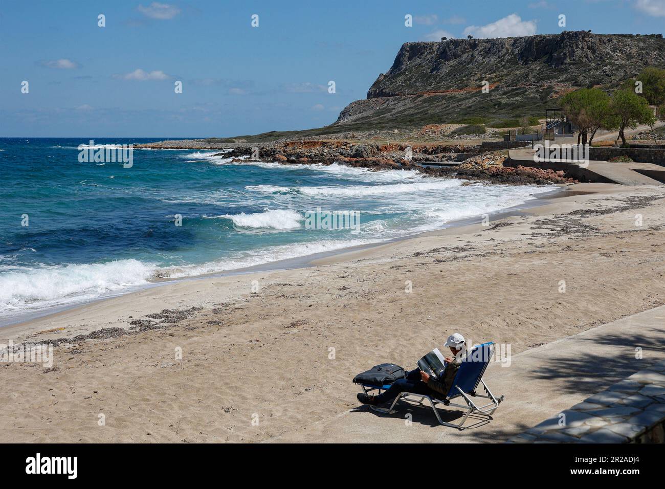 Uomo anziano che si rilassa mentre si siede sulle sedie pieghevoli in spiaggia leggendo una rivista, Kalimera Kriti spiaggia, Sissi, Creta, Grecia Foto Stock