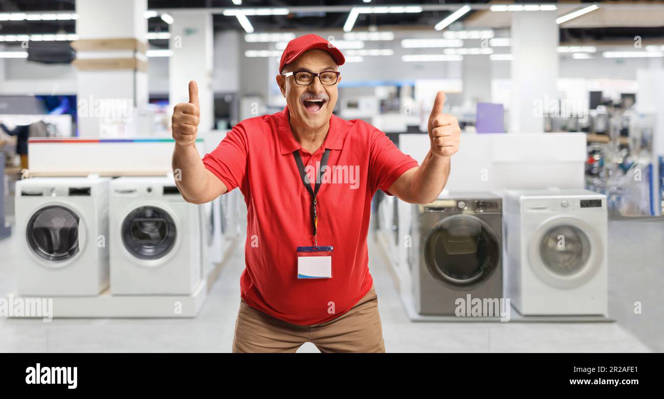 Un venditore maturo entusiasta che gesta i pollici all'interno di un negozio di elettrodomestici Foto Stock