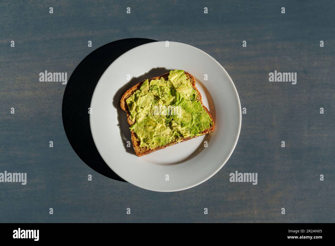 Brindisi all'avocado su un piatto bianco seduto su un piano di cemento alla luce del sole con ombre dure Foto Stock