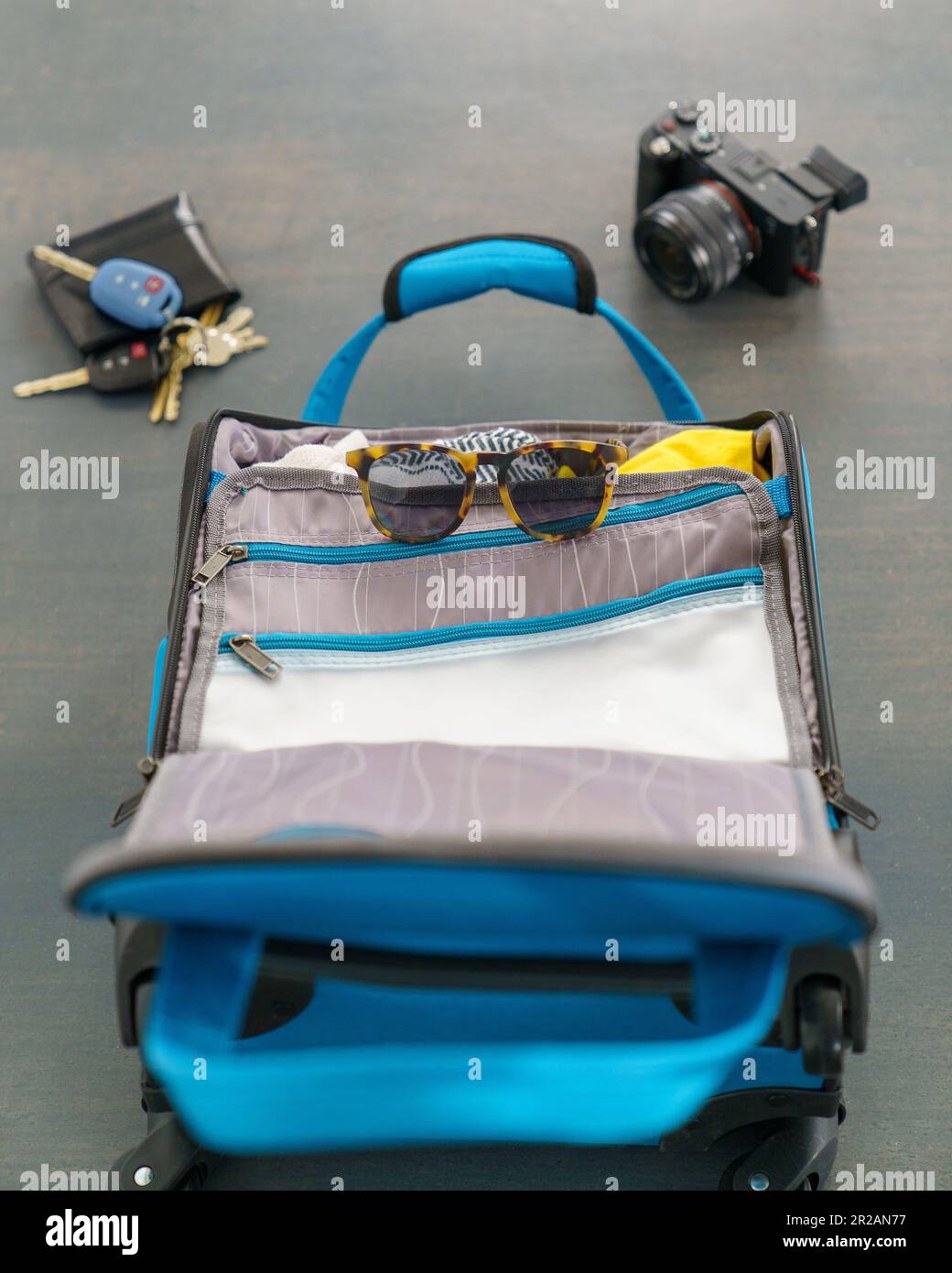 Piccola borsa blu con occhiali da sole, fotocamera, portafoglio e chiavi per una vacanza breve. Posa su un pavimento in cemento. Foto Stock