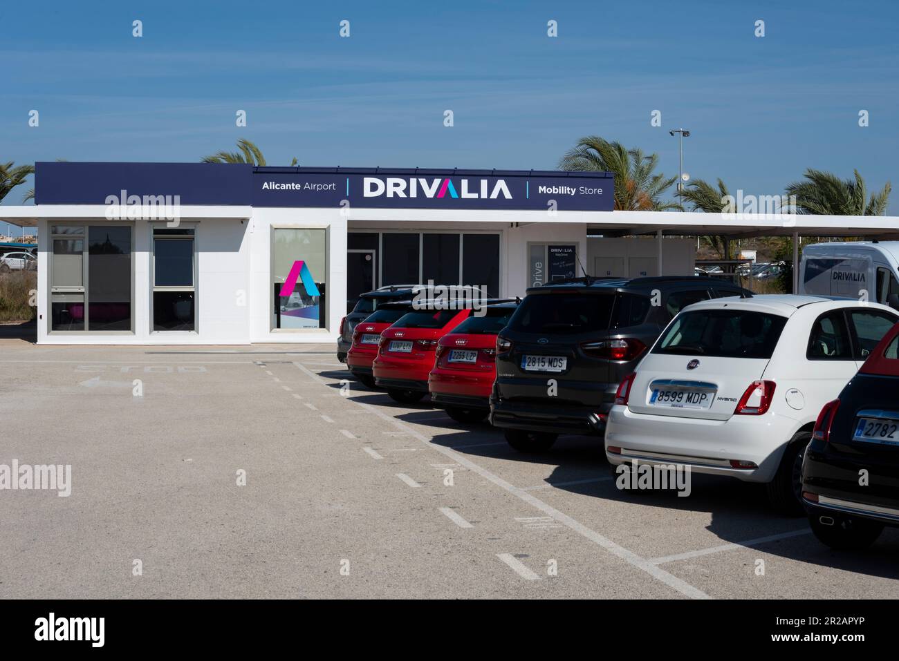 Noleggio auto Drivalia presso l'aeroporto di Alicante, Spagna. Noleggio auto, con auto a noleggio parcheggiate. Cielo blu. Varie dimensioni di auto a noleggio Foto Stock