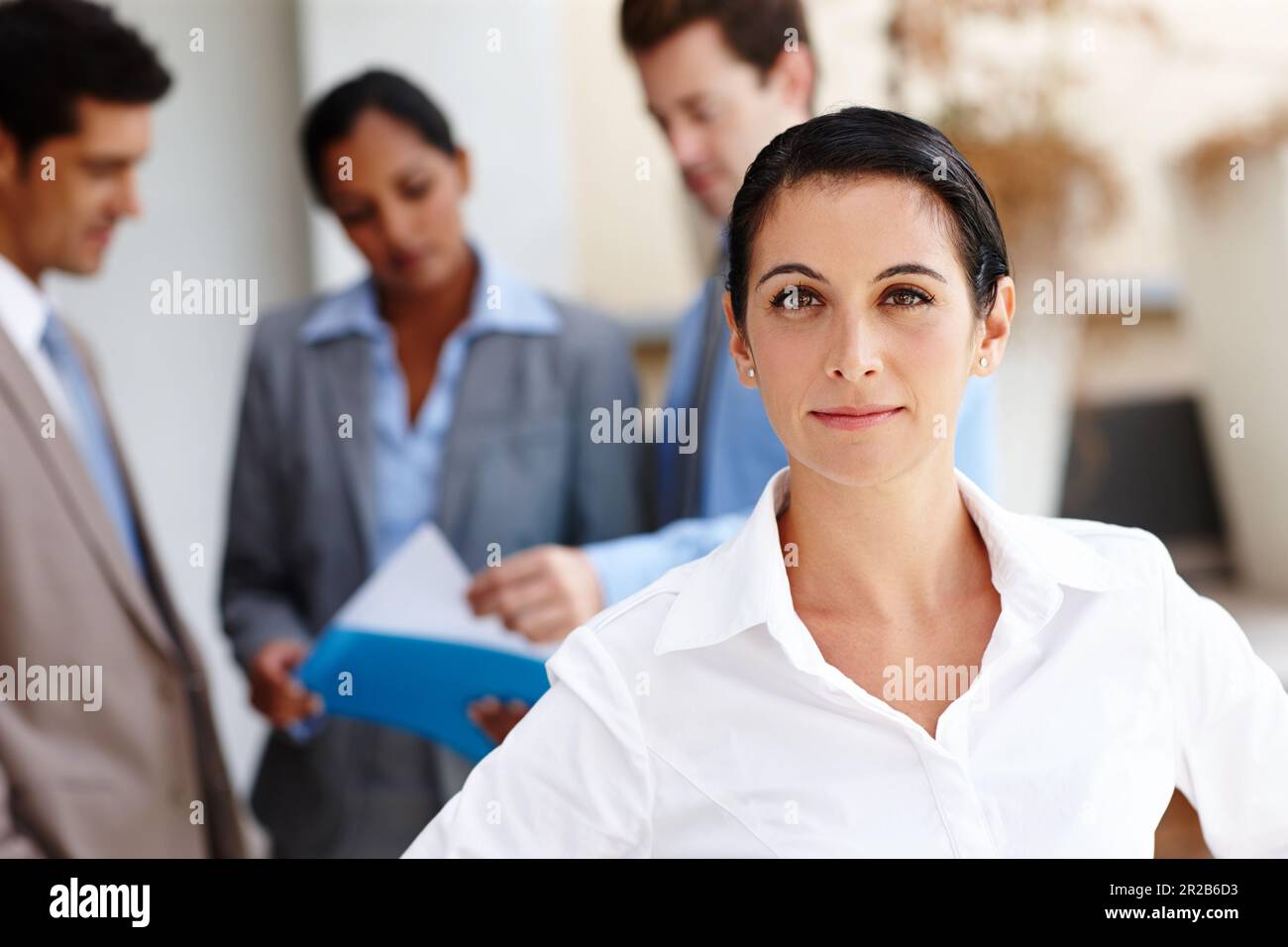 Shes serio circa successo. Ritratto di una bella giovane donna d'affari con i suoi colleghi sfocato sullo sfondo. Foto Stock