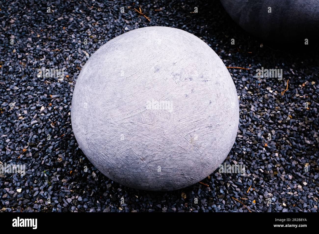 Una pietra rotonda riposa pacificamente nel vasto campo, una meraviglia naturale in mezzo al paesaggio aperto. Lisci e lucidati nel tempo. Foto Stock