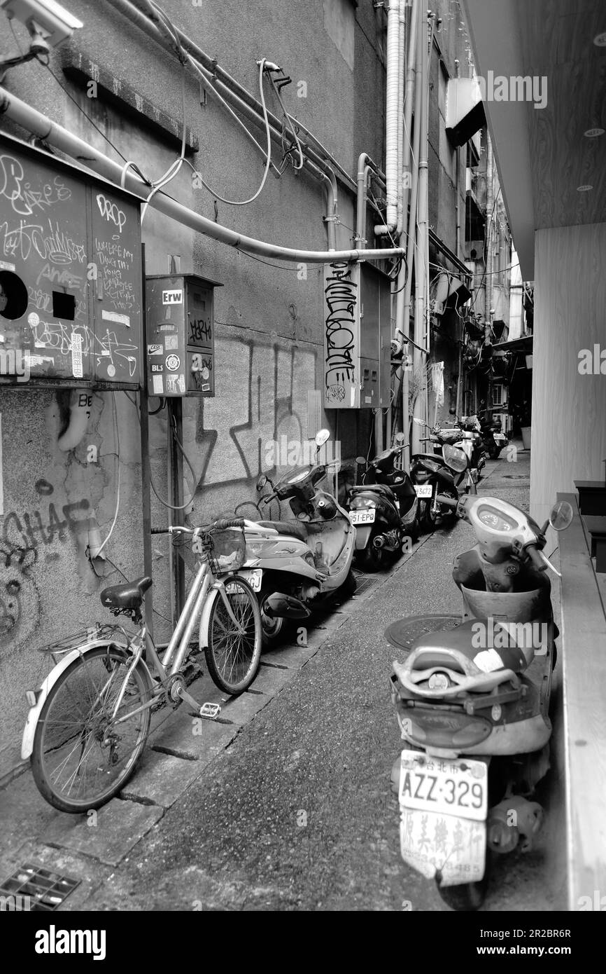 Vicolo stretto tra gli edifici di Taipei, Taiwan; biciclette parcheggiate e scooter; graffiti e adesivi sulle scatole fusibili dei contatori elettrici e a parete. Foto Stock