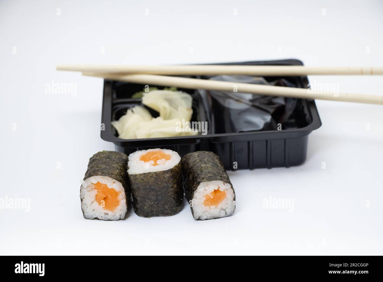 sushi con salmone accanto al confezionamento di alimenti in plastica su sfondo bianco, consegna a domicilio Foto Stock