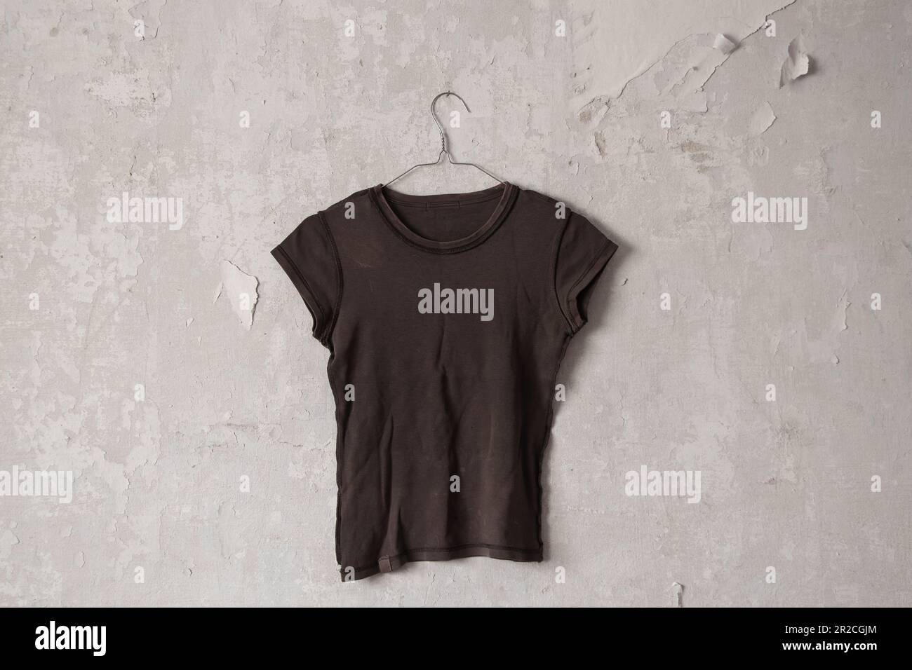 t-shirt femmina marrone appesa a un appendiabiti su un vecchio muro bianco sporco a casa Foto Stock