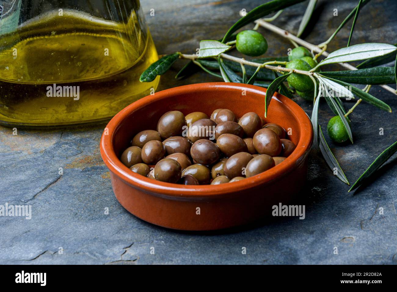 Olive in un piatto di argilla, fotografia studio con sfondo di pietra. Vita morta con il ramo d'oliva e le olive crude. Foto Stock