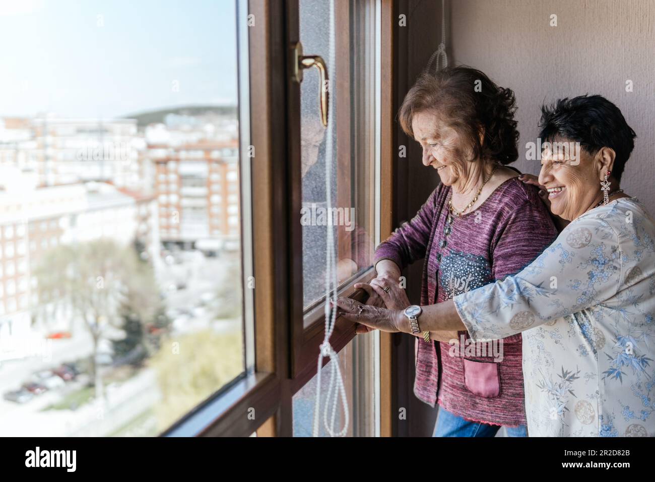 due giovani donne che guardano fuori dalla finestra della loro casa Foto Stock