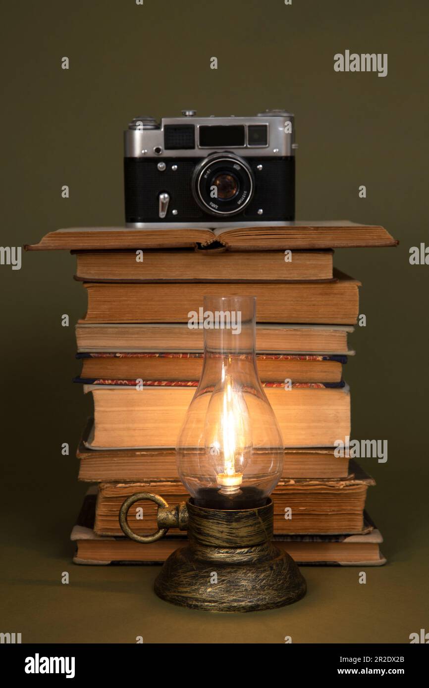 Libri antichi e una lampada a mano con lampadina, stilizzata come antica. C'è una vecchia macchina fotografica in cima ai libri. Oggetti collocati su uno sfondo di oliva. Foto Stock