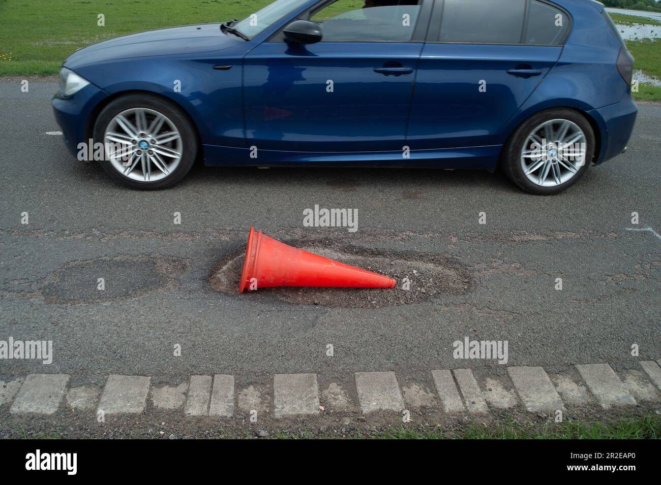 Dorney, Buckinghamshire, Regno Unito. 19th maggio, 2023. Anche se alcuni buche sono state patched nel vicino villaggio rurale di Dorney REACH nel Buckinghamshire oggi, ci sono ancora un certo numero di buche sulla strada comune nel Dorney Village che hanno ancora bisogno di riparare. Questo ha un cono di avvertimento da esso ma continua ad essere bussato sopra passando il traffico. Buckinghamshire ha migliaia di buche non riparate che vengono lentamente applicate con una nuova macchina Velocity Patcher. Credit: Maureen McLean/Alamy Live News Foto Stock