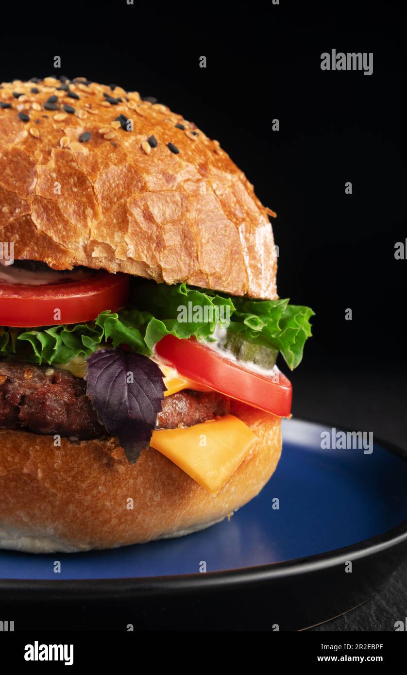 Delizioso cheeseburger con lattuga, pomodoro e formaggio su sfondo nero. Foto Stock
