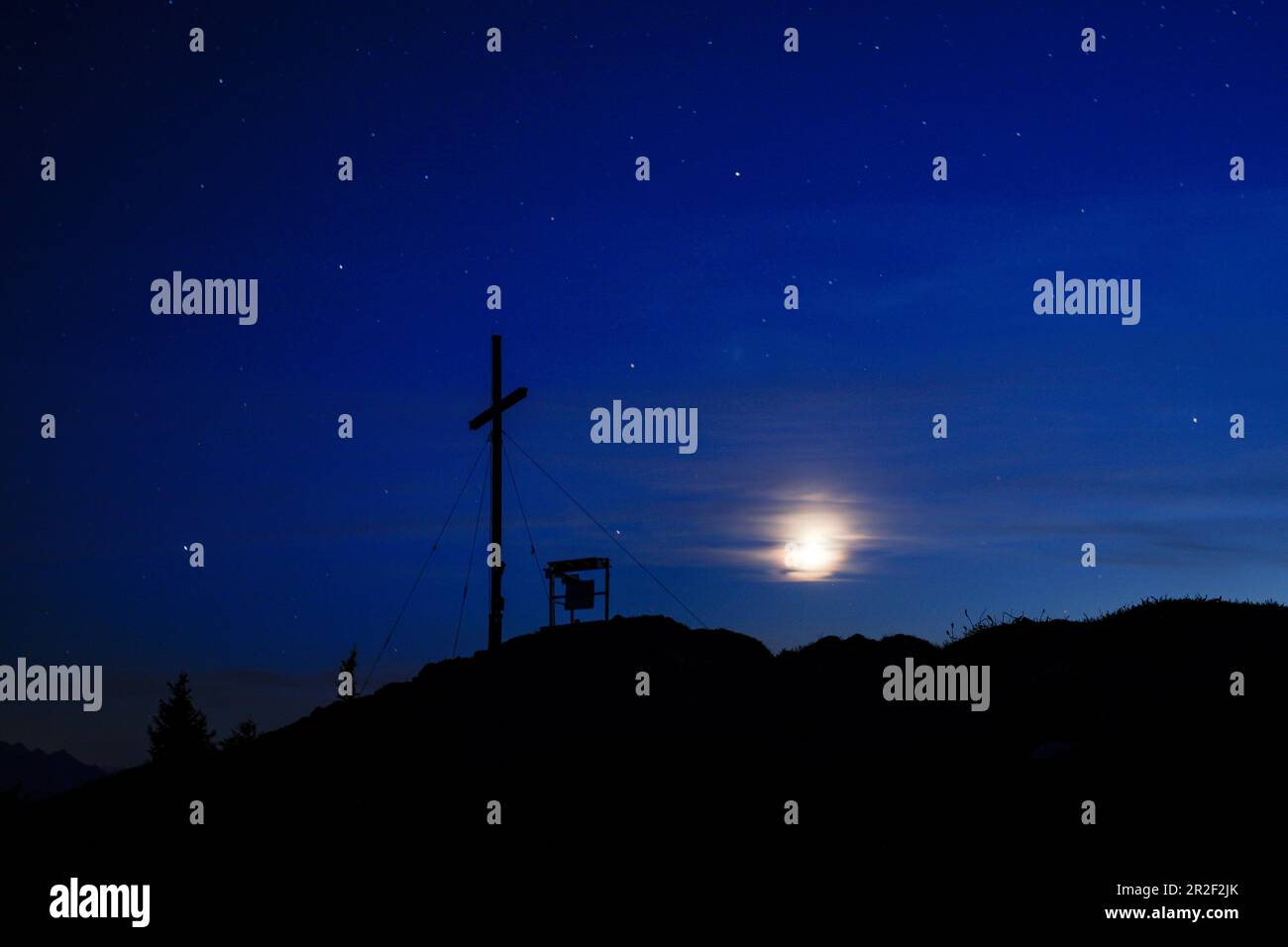 Croce sommitale del Jochberg di notte con nuvole, stelle e luna Foto Stock