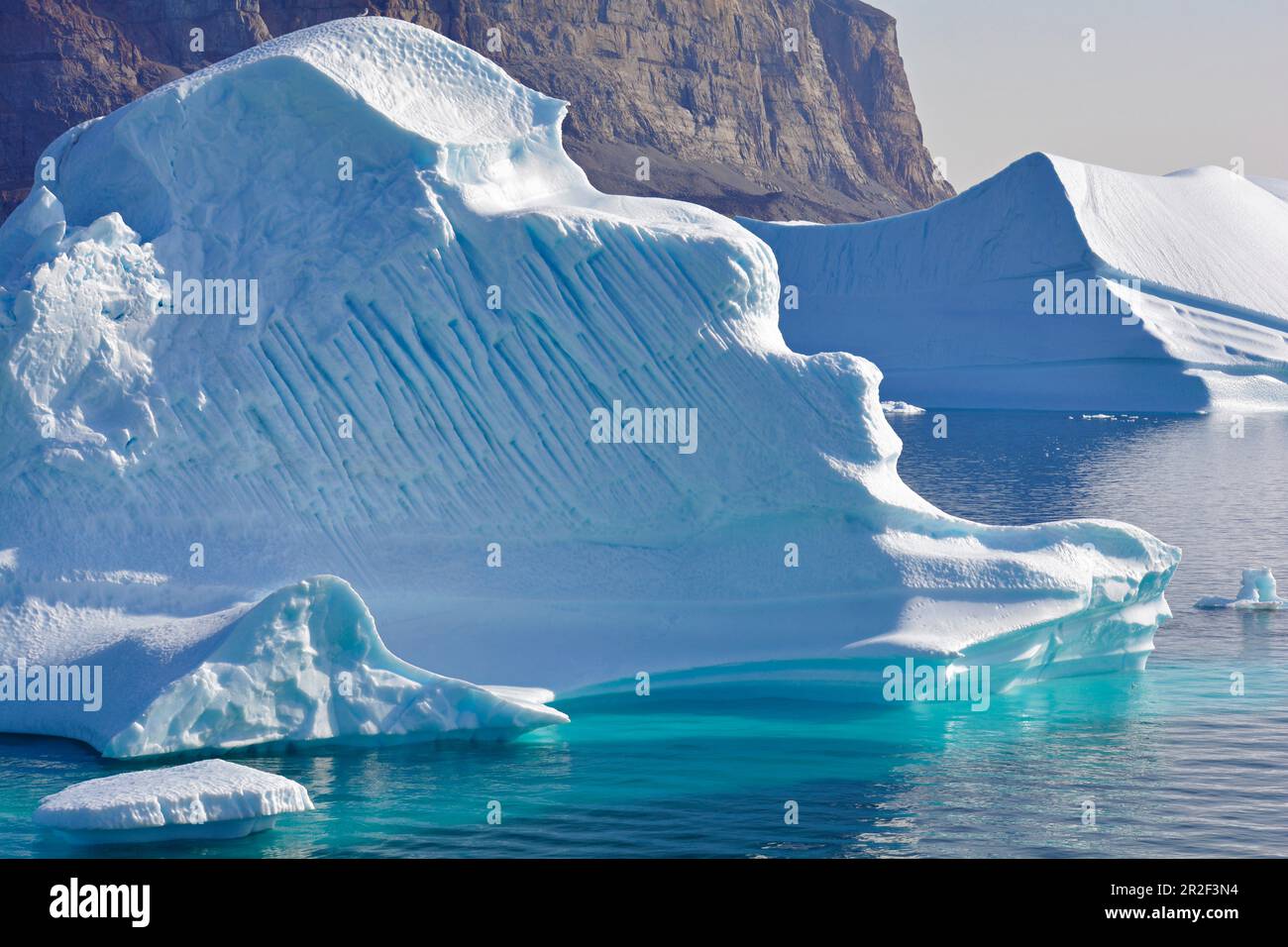 Iceberg al largo di Uummannaq nella Groenlandia occidentale; superfici e strutture diverse; ghiaccio sott'acqua risplende intensamente turchese; ripido, parete rocciosa di montagna in th Foto Stock