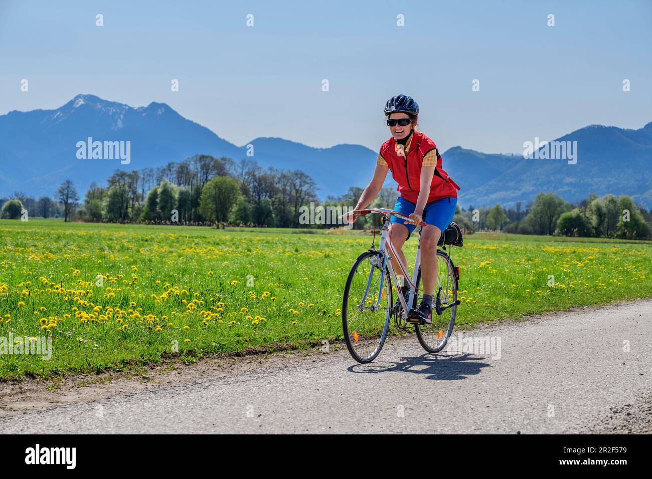 Donna in bicicletta con Hochgern sullo sfondo, Chiemsee Cycle Path, Chiemgau, alta Baviera, Baviera, Germania Foto Stock