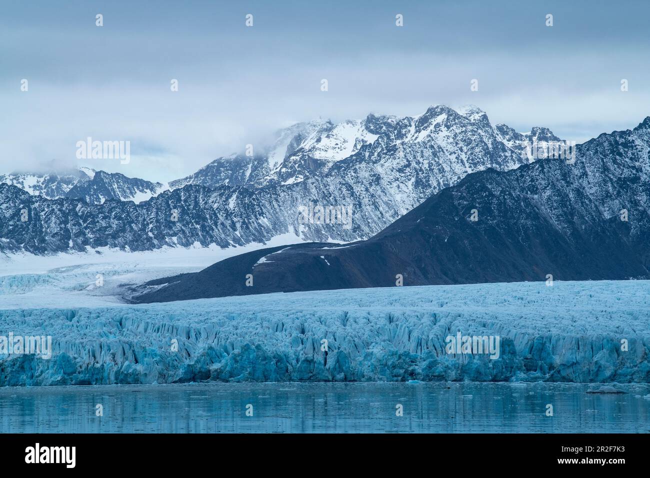 Scena grafica di aspre montagne innevate e un ampio ghiacciaio che si estende fino al mare, Lilliehöökfjord, Albert i Land, Spitsbergen, Norvegia, Euro Foto Stock