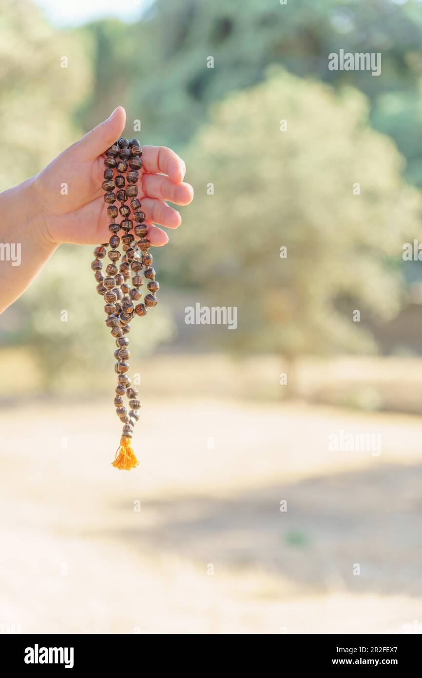 Le mani di una donna che tiene una japa mala indù illuminata dal sole in meditazione nella campagna al tramonto Foto Stock