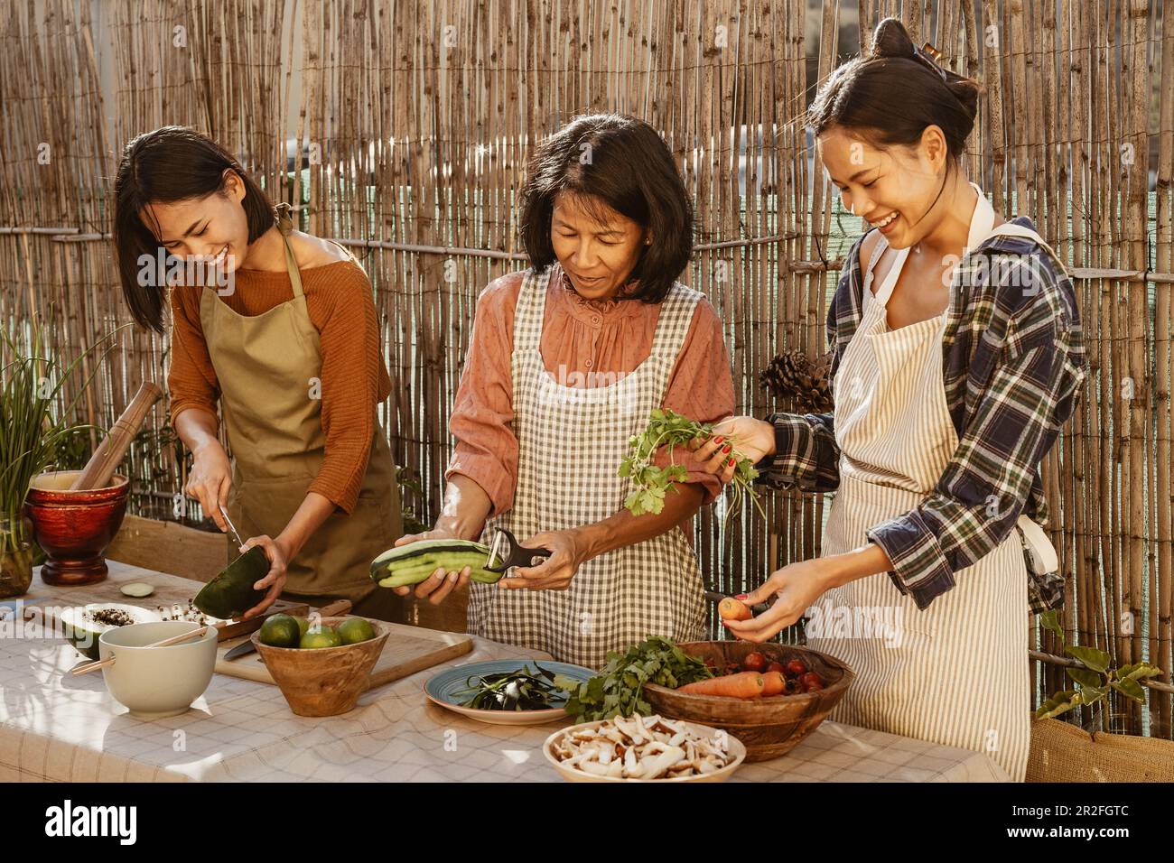 Felice famiglia del sud-est asiatico divertirsi a preparare la ricetta del cibo tailandese insieme nel patio della casa Foto Stock