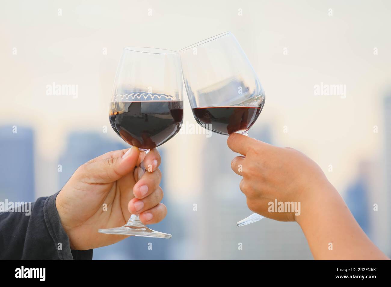 mani che tengono il bicchiere di vino rosso sul balcone durante il tramonto, concetto di celebrazione Foto Stock