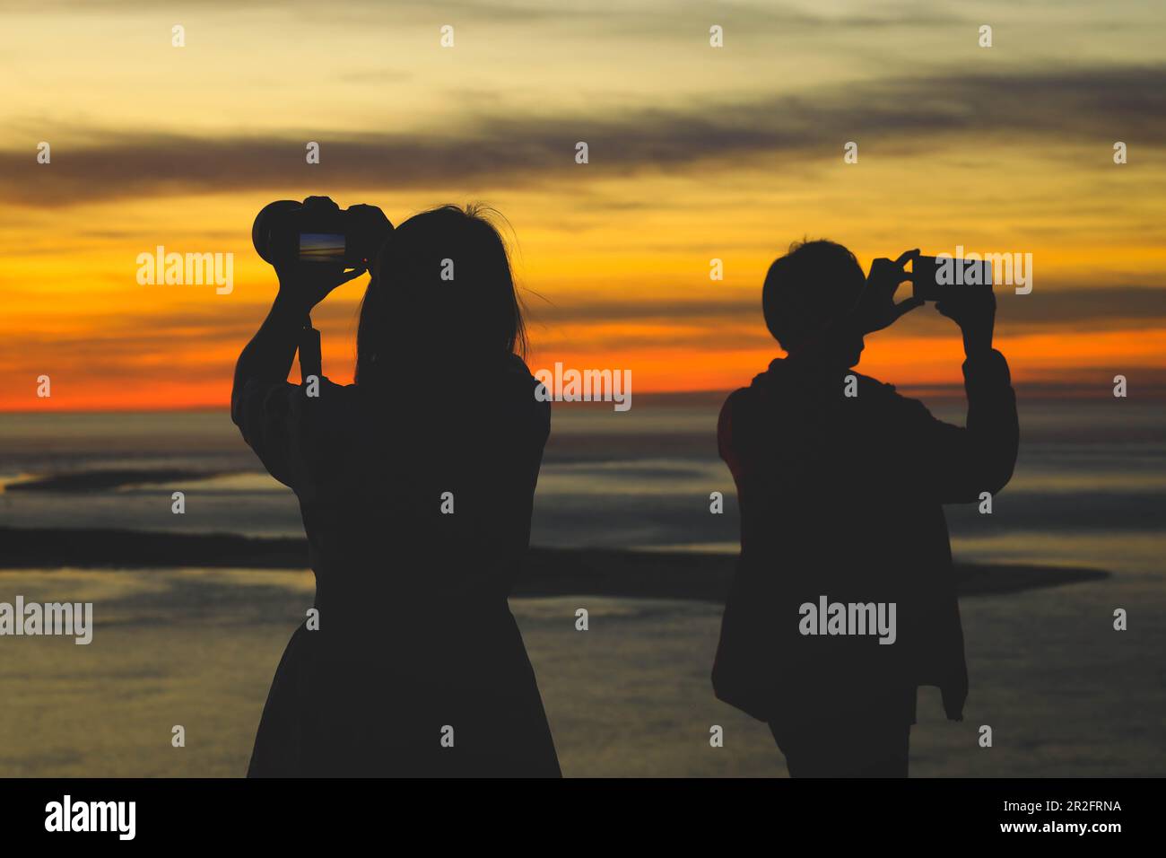 Silhouette di donna che tiene la fotocamera a scattare foto con la sua amica durante l'alba o il tramonto Foto Stock