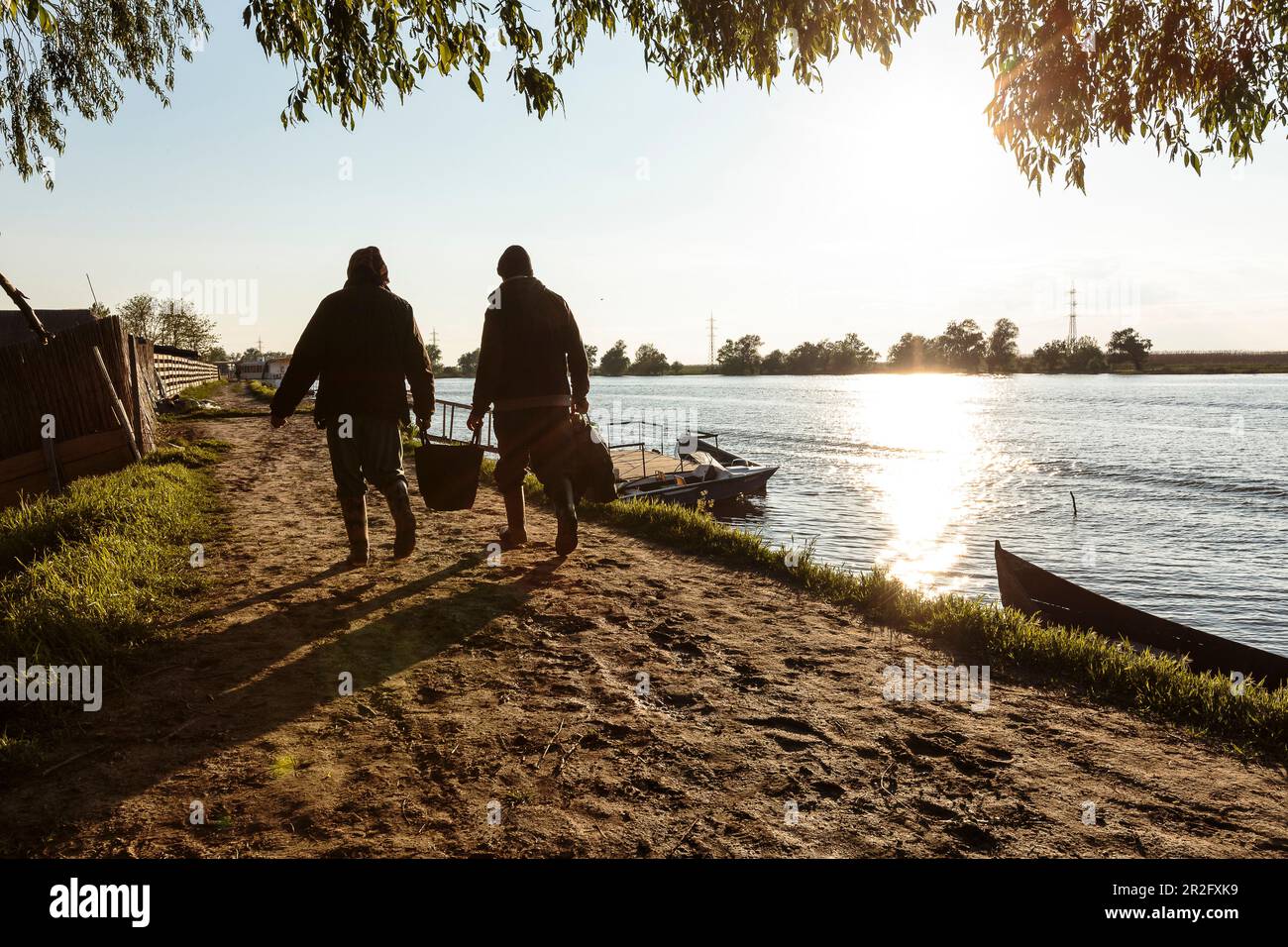 Il Delta del Danubio, una vecchia coppia, porta lo shopping lungo il sentiero lungo il fiume al sole serale, Mila 23, Tulcea, Romania. Foto Stock