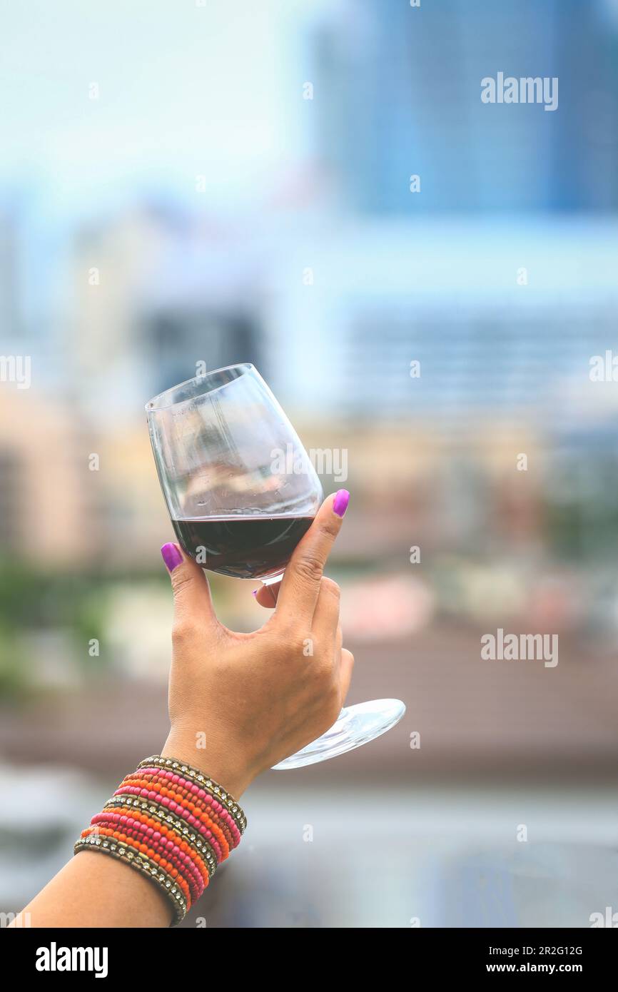 primo piano sulle mani del womon che tiene bicchieri di vino rosso sul balcone durante il tramonto, concetto di celebrazione Foto Stock
