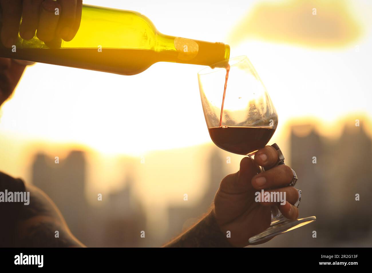 Bicchiere e bottiglia di vino rosso con attenzione selettiva su bicchiere di vino, versando vino rosso al tramonto Foto Stock