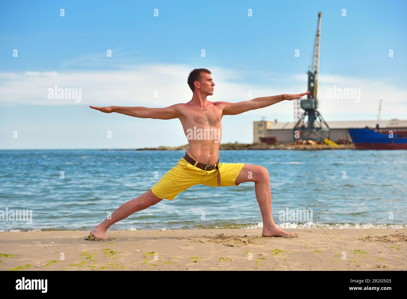 uomo che fa esercizi di yoga sulla spiaggia su sfondo gru porto Foto Stock