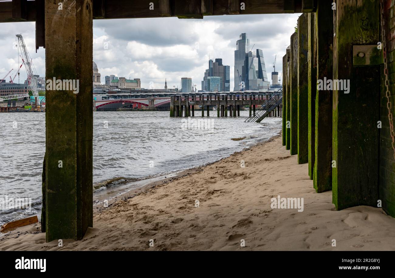 Londra. UK- 05.17.2023. Una vista da sotto il molo della Spiaggia del Tamigi sulla riva sud del Tamigi con una vista dei grattacieli nel Cit Foto Stock