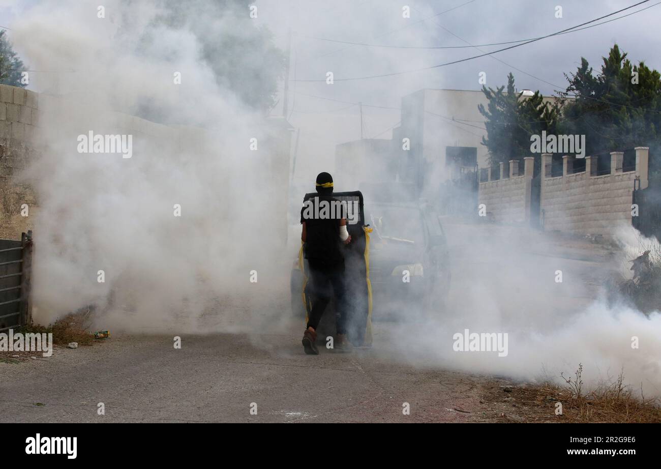 Kufr Qadoom, Nablus. 19th maggio, 2023. Un protester palestinese è visto nel fumo di barattoli di gas lacrimogeno sparati dai soldati israeliani durante gli scontri a seguito di una protesta contro l'espansione degli insediamenti ebrei nel villaggio di Kufr Qadoom, vicino a Nablus, il 19 maggio 2023. Credit: Nidal Eshtayeh/Xinhua/Alamy Live News Foto Stock