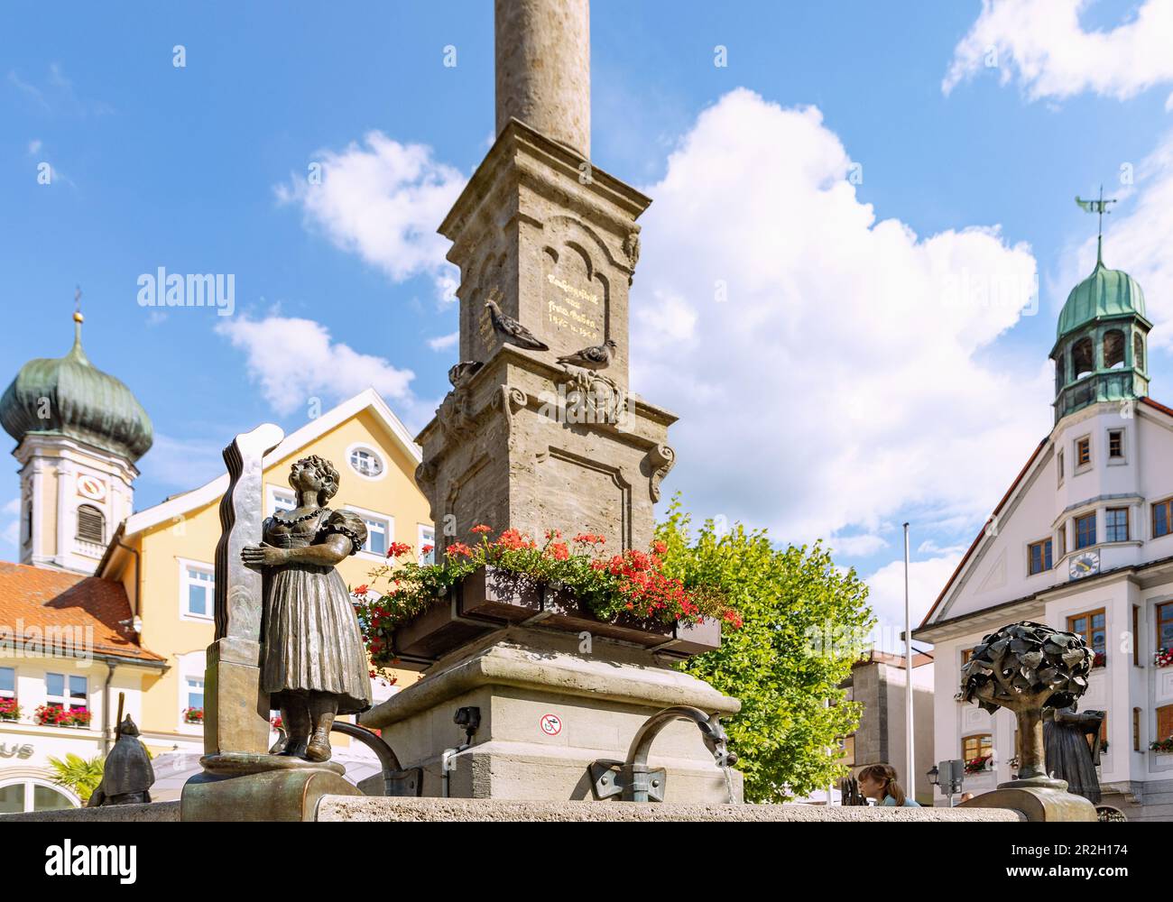 Fontana con figura bronzea della calza e colonna mariana a Marienplatz con la chiesa parrocchiale di San Nicholas e il municipio di Immenstadt im Foto Stock