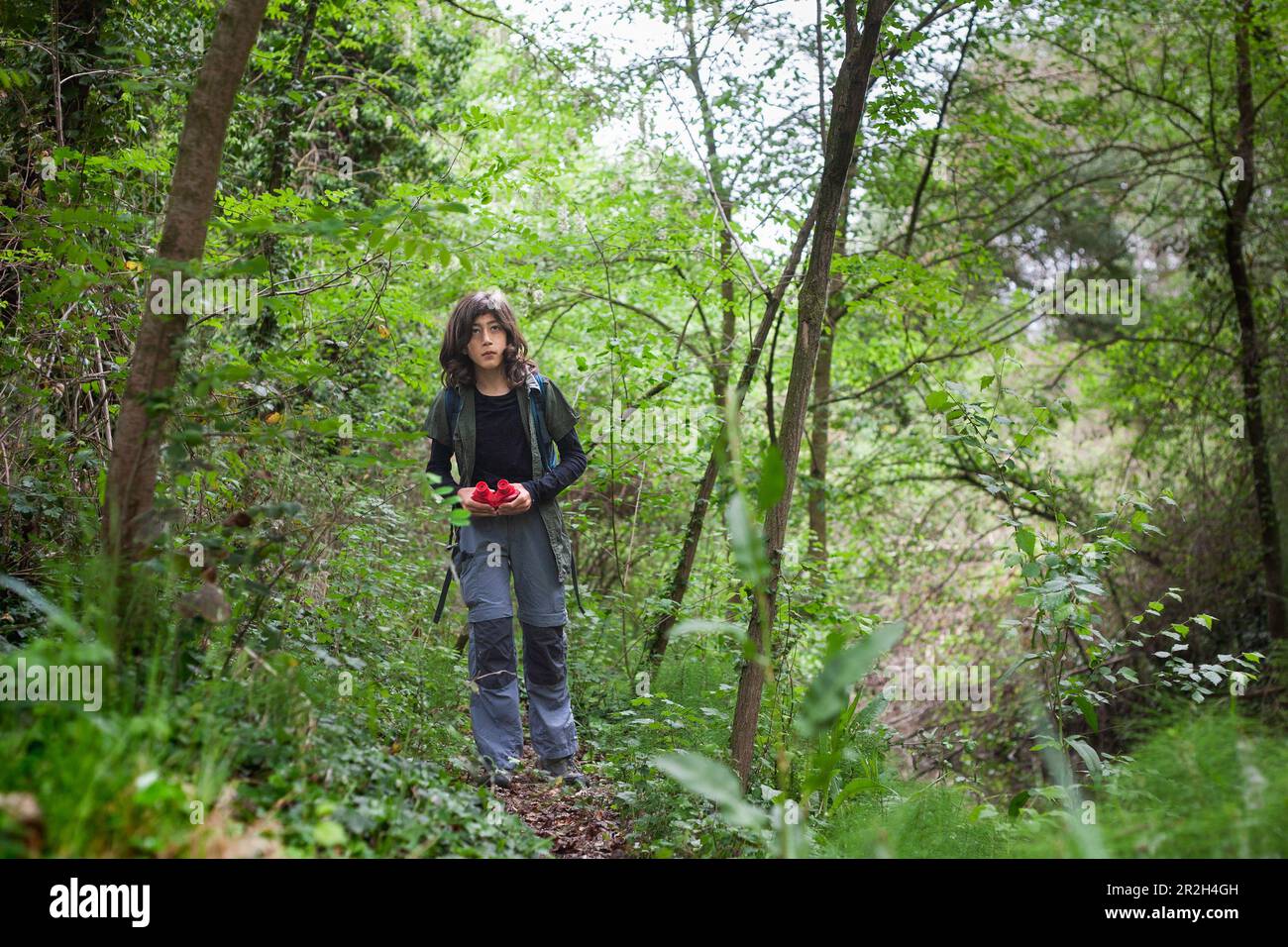 Unisciti a un ragazzo di 11 anni mentre cammina ed esplora la foresta, dotato di binocoli, scoprendo le meraviglie della natura. Foto Stock