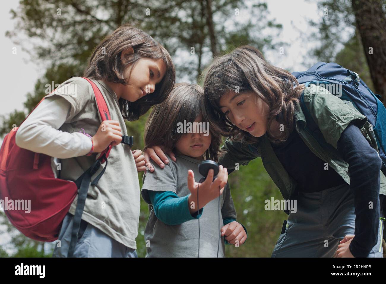Tre bambini sono in una foresta, consultando una bussola per navigare e trovare la loro strada. Foto Stock