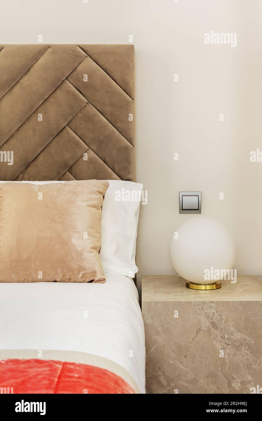 Particolare di una camera da letto decorata con un cubo di marmo, una lampada rotonda e una testata imbottita in velluto marrone chiaro Foto Stock