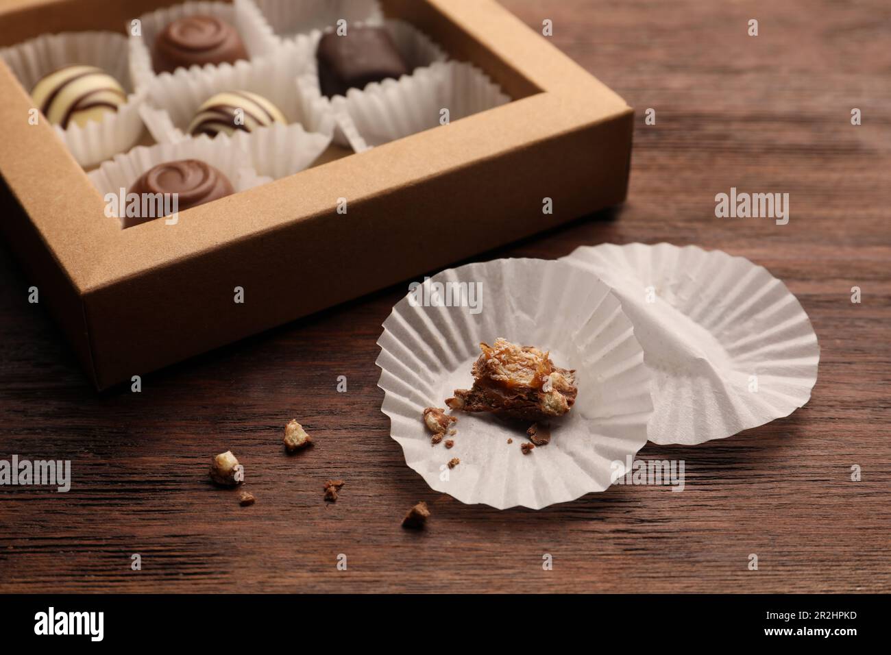 Bicchieri di carta caramella vicino a scatola parzialmente vuota di dolci al cioccolato su tavola di legno, primo piano Foto Stock