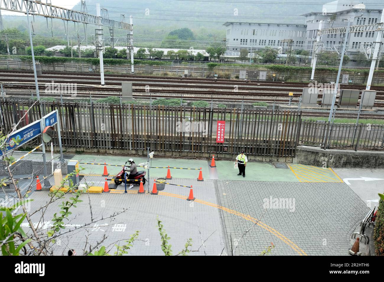 Ingresso al garage con pista per motociclette, scooter, ufficiale di polizia e binari ferroviari sul retro; Shin Kong Mitsukoshi, Kaohsiung, Taiwan. Foto Stock