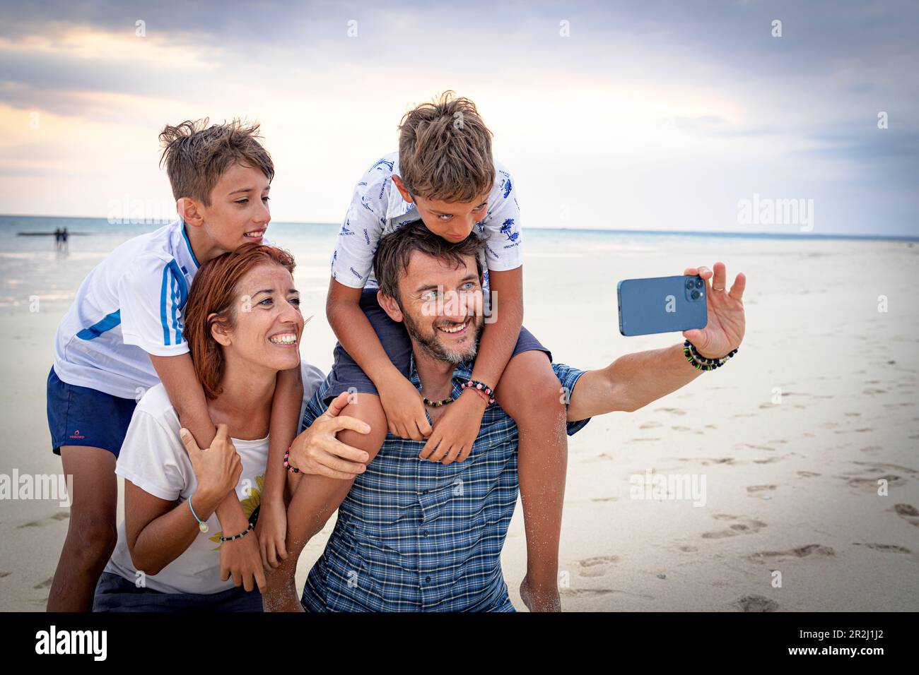 Famiglia felice con due ragazzi che scattano un selfie con smartphone su una spiaggia, Zanzibar, Tanzania, Africa orientale, Africa Foto Stock