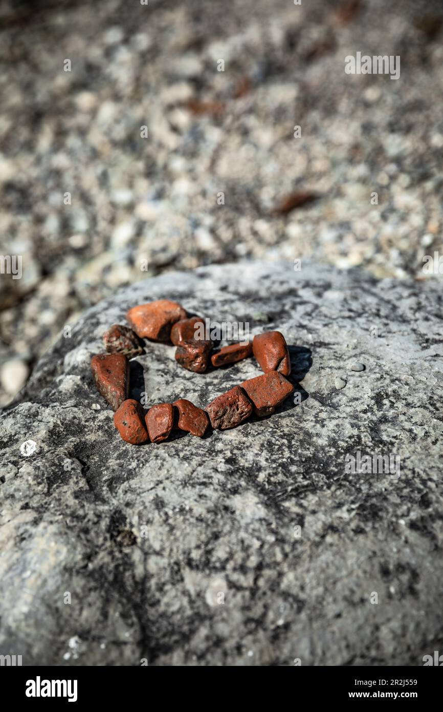 Un cuore fatto di piccole pietre rosse su una grande pietra sulla spiaggia Foto Stock