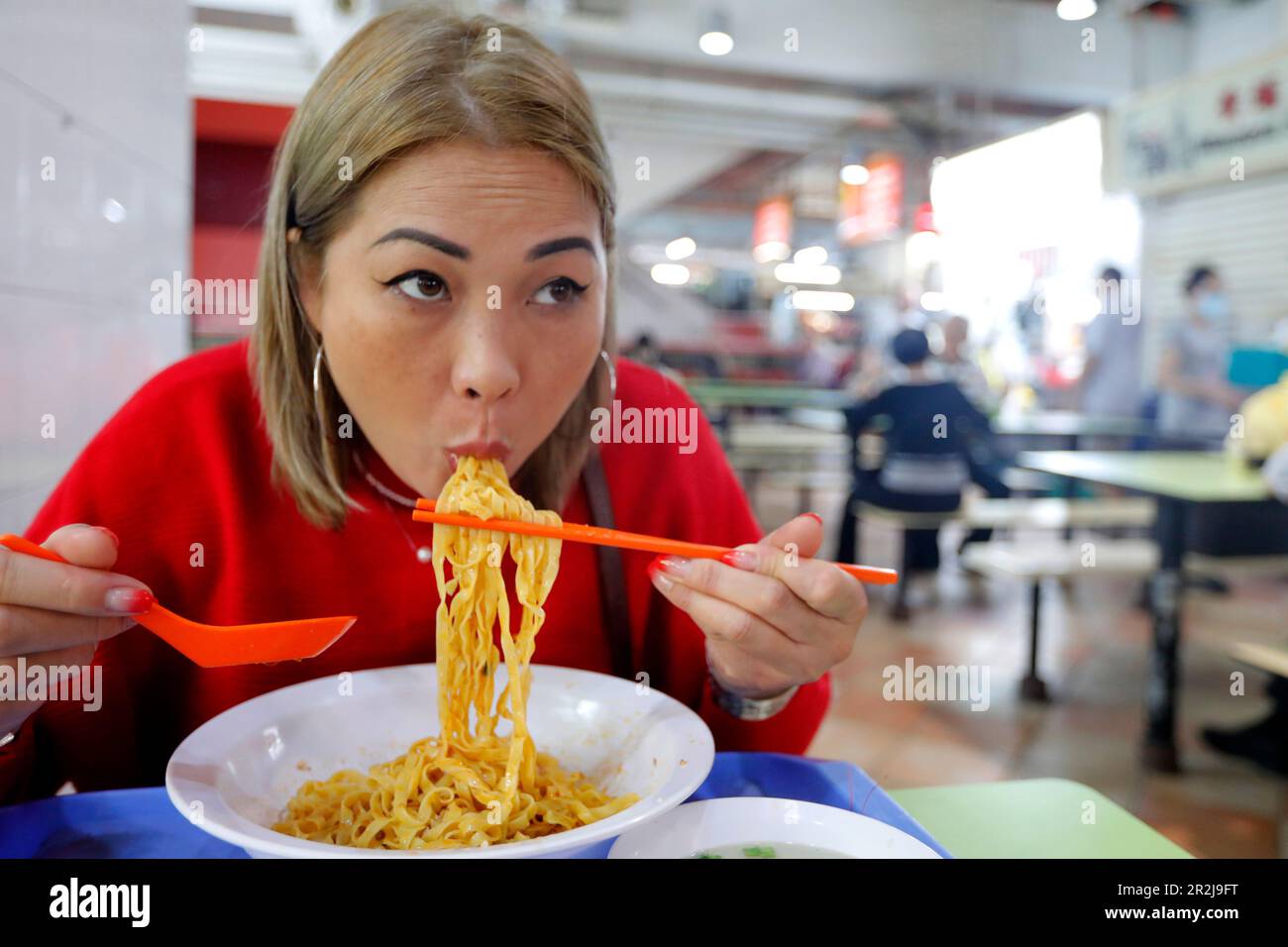 Giovane donna che mangia presso la tradizionale bancarella di cibo Asiatico nel centro dei falchi del Singapore Food Trail, Singapore, Asia sudorientale Foto Stock