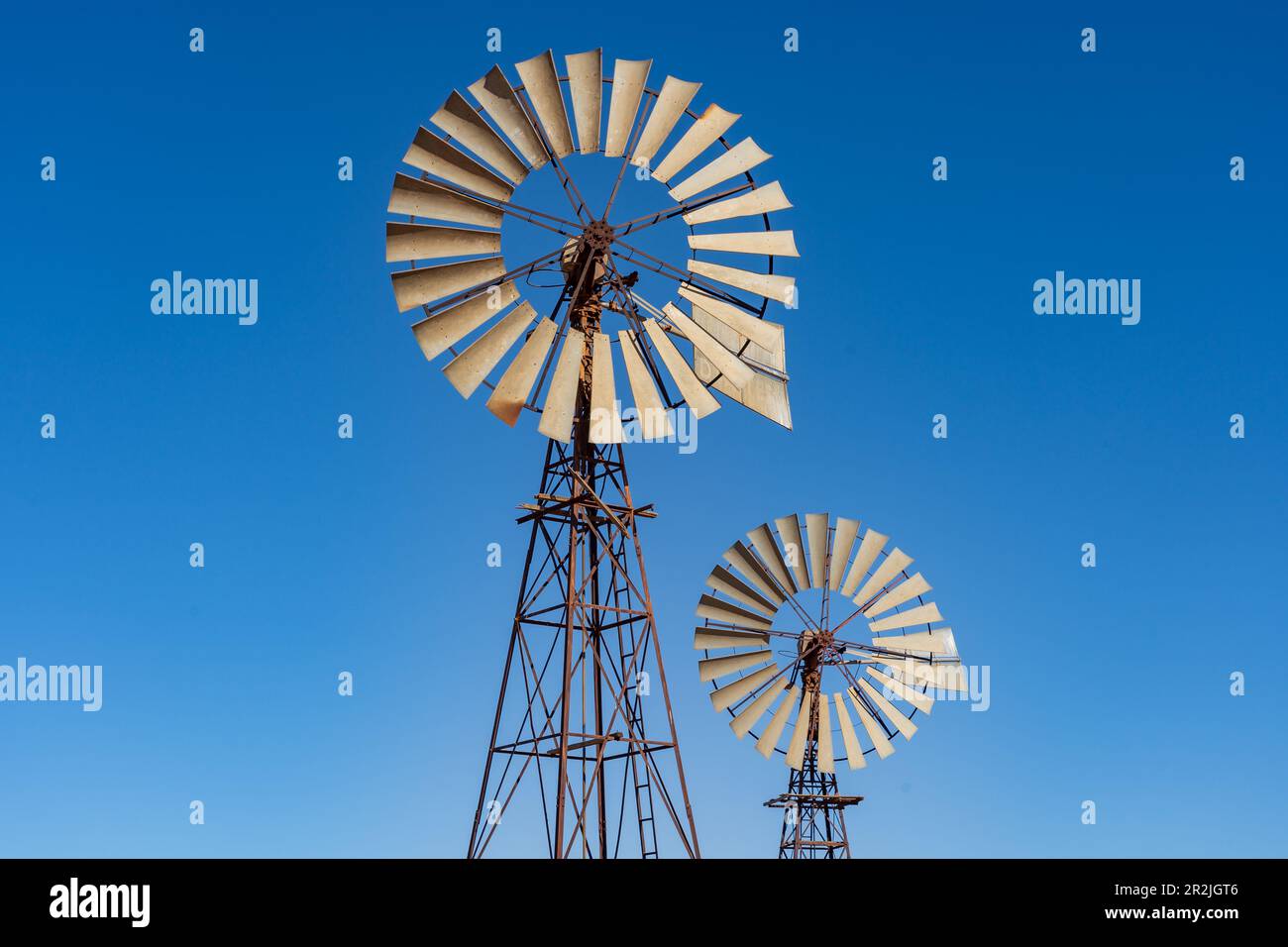 Guardando in alto due grandi mulini a vento contro un cielo blu chiaro vicino a Broken Hill nell'Outback New South Wales, Australia. Foto Stock