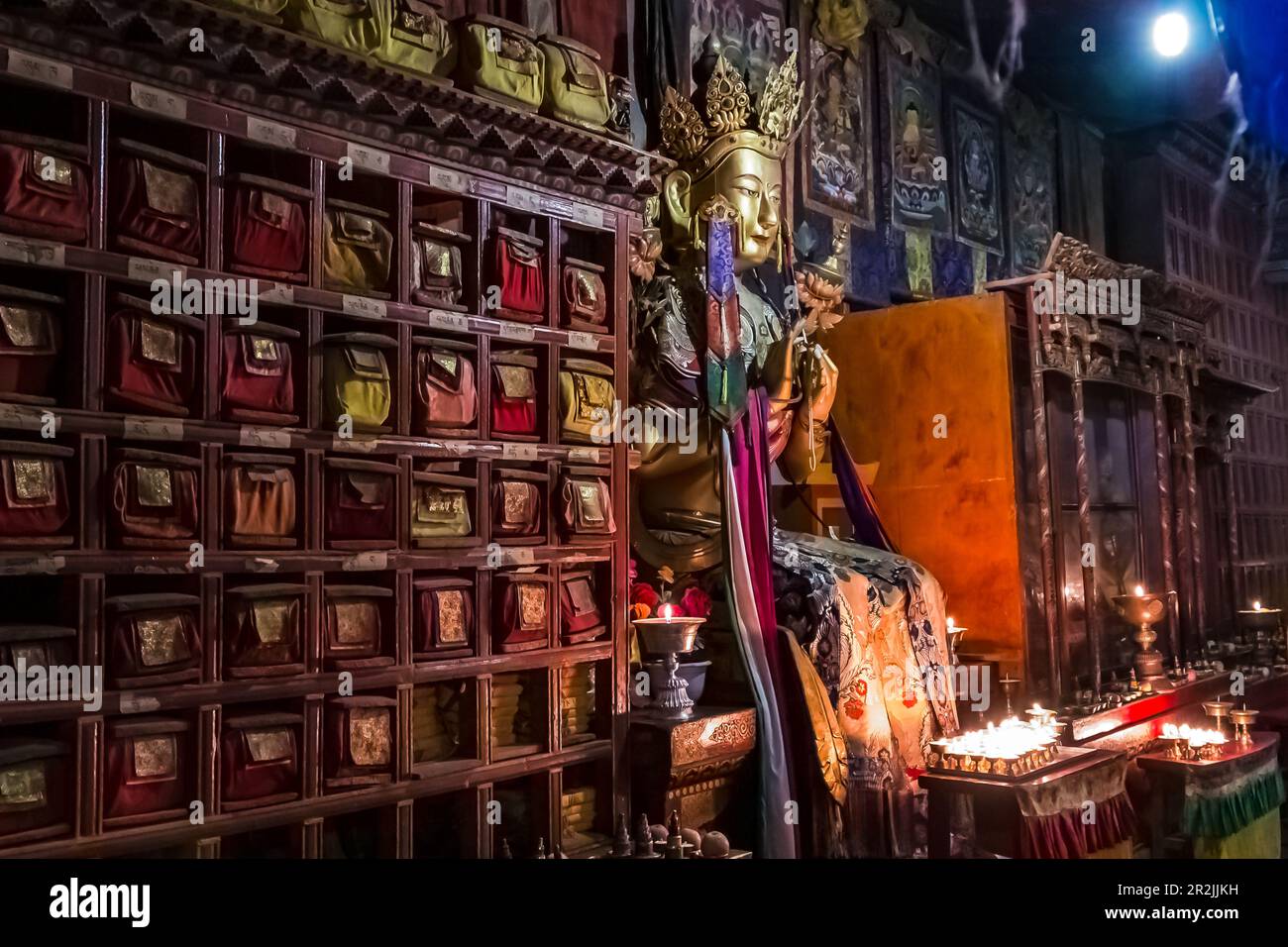 Figura di Buddha e antica unità da parete con candele e offerte all'interno scuro di una sala di preghiera al Monastero di Kumbum Champa Ling, Xining, Cina Foto Stock